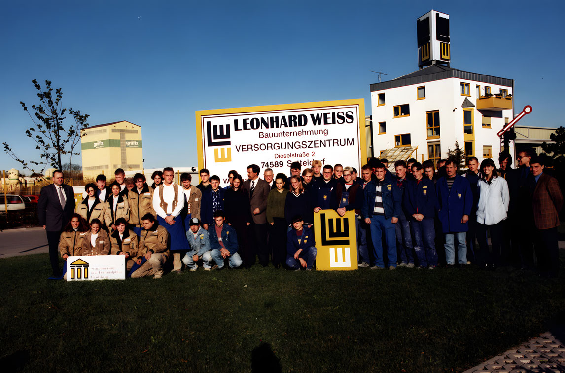 Farbaufnahme einer Gruppe von Auszubildenden und Mitarbeitern vor dem Versorgungszentrum von LEONHARD WEISS in Satteldorf