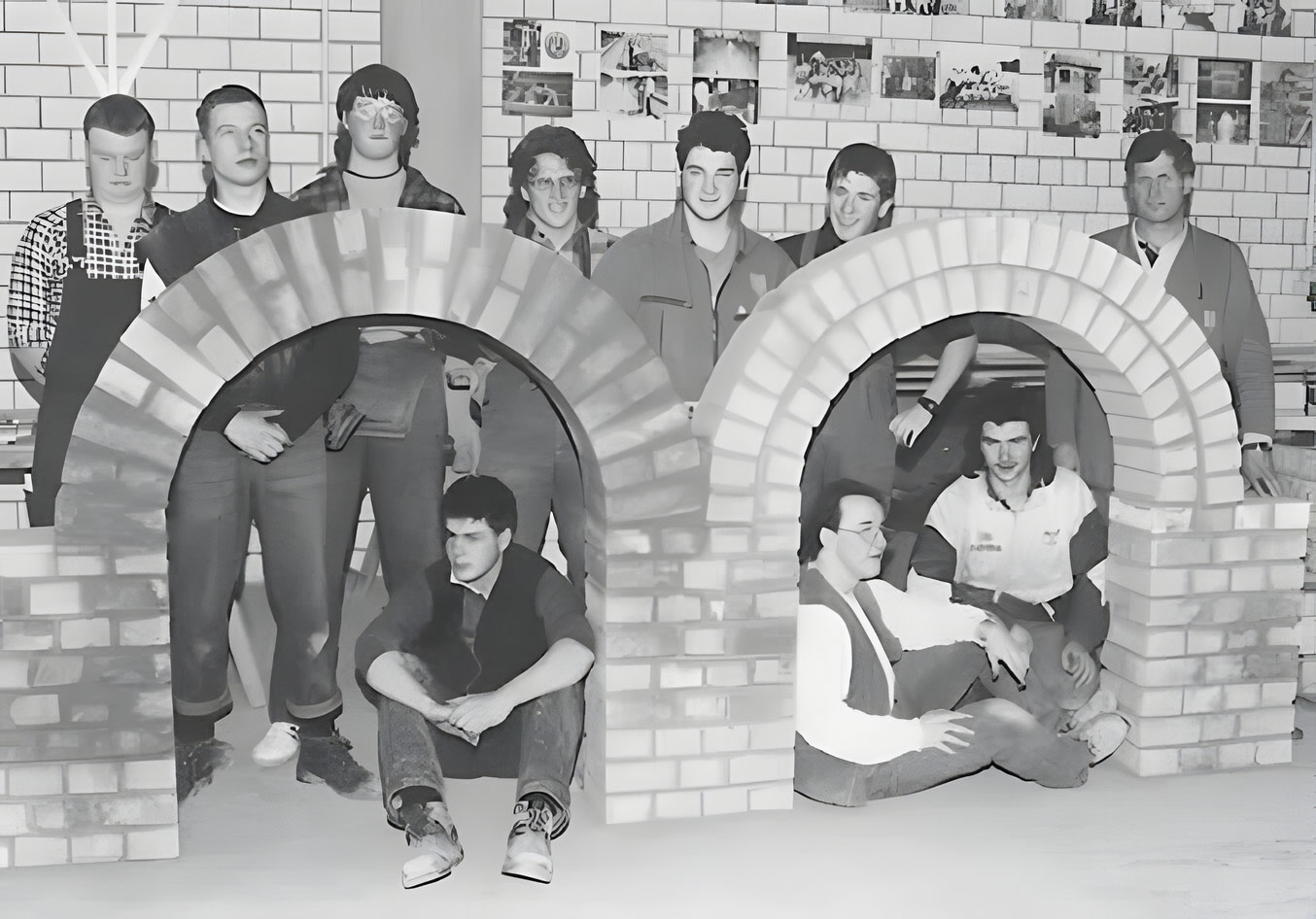 Schwarz-Weiß-Bild einer Gruppe von jungen Männern in Arbeitskleidung, die stolz vor gemauerten Rundbögen posieren
