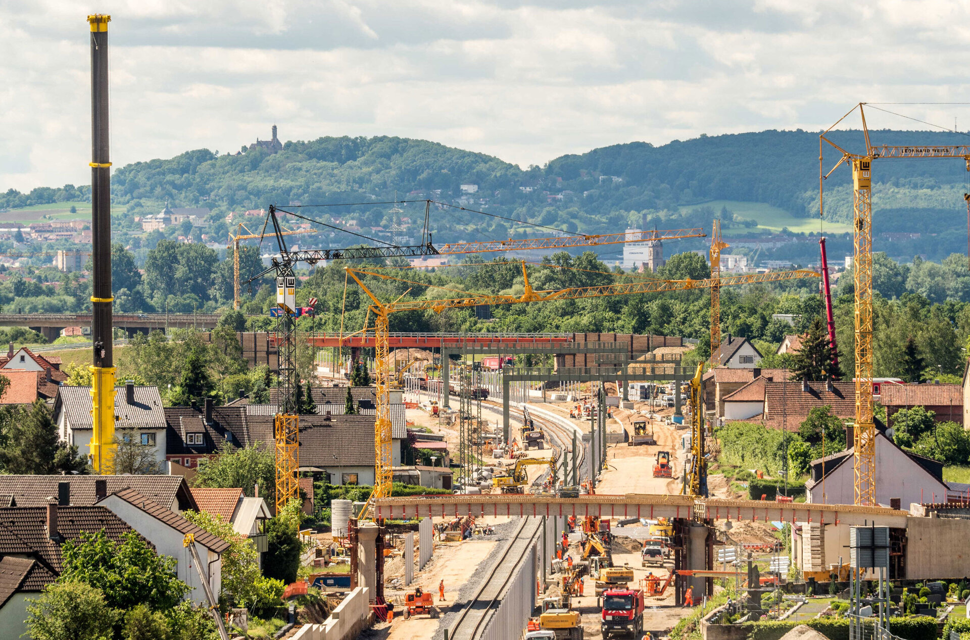 Baustelle in Zapfendorf mit zahlreichen Kränen, Baugeräten und einer Brücke, umgeben von Häusern und grüner Landschaft