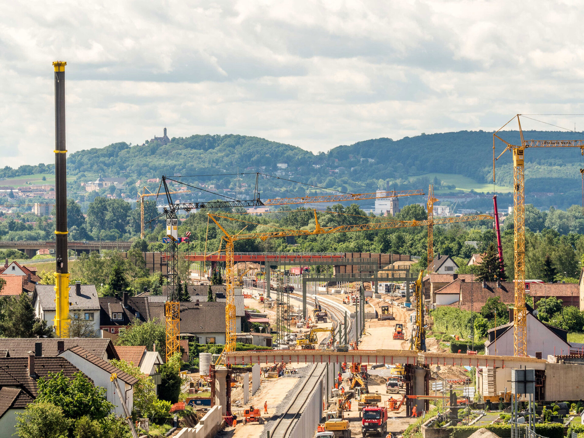 Baustelle in Zapfendorf mit zahlreichen Kränen, Baugeräten und einer Brücke, umgeben von Häusern und grüner Landschaft