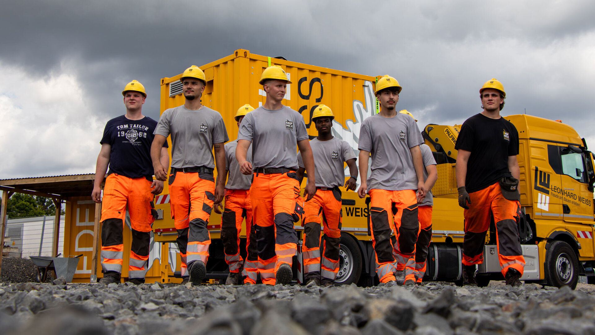 Group of trainees with yellow helmets and work clothes walk towards the camera