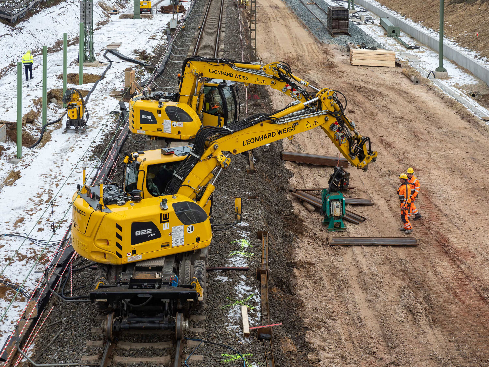 Baustelle in Hallstadt mit gelben Baggern von LEONHARD WEISS, Arbeiter in Sicherheitskleidung und schneebedecktem Boden