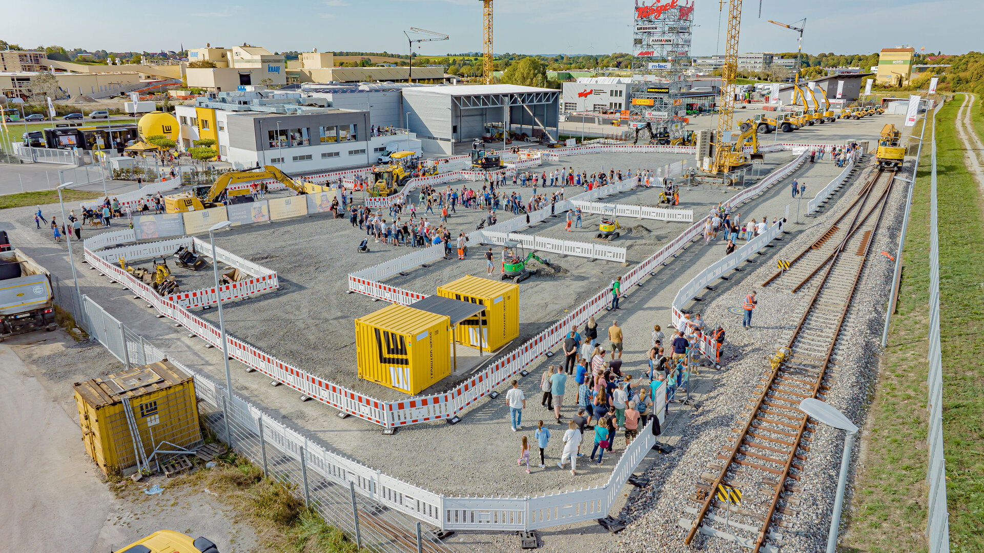 Das LEONHARD WEISS Trainingszentrum mit Übungsbereich, Bahngleisen, Baumaschinen und Besuchern bei einer Veranstaltung