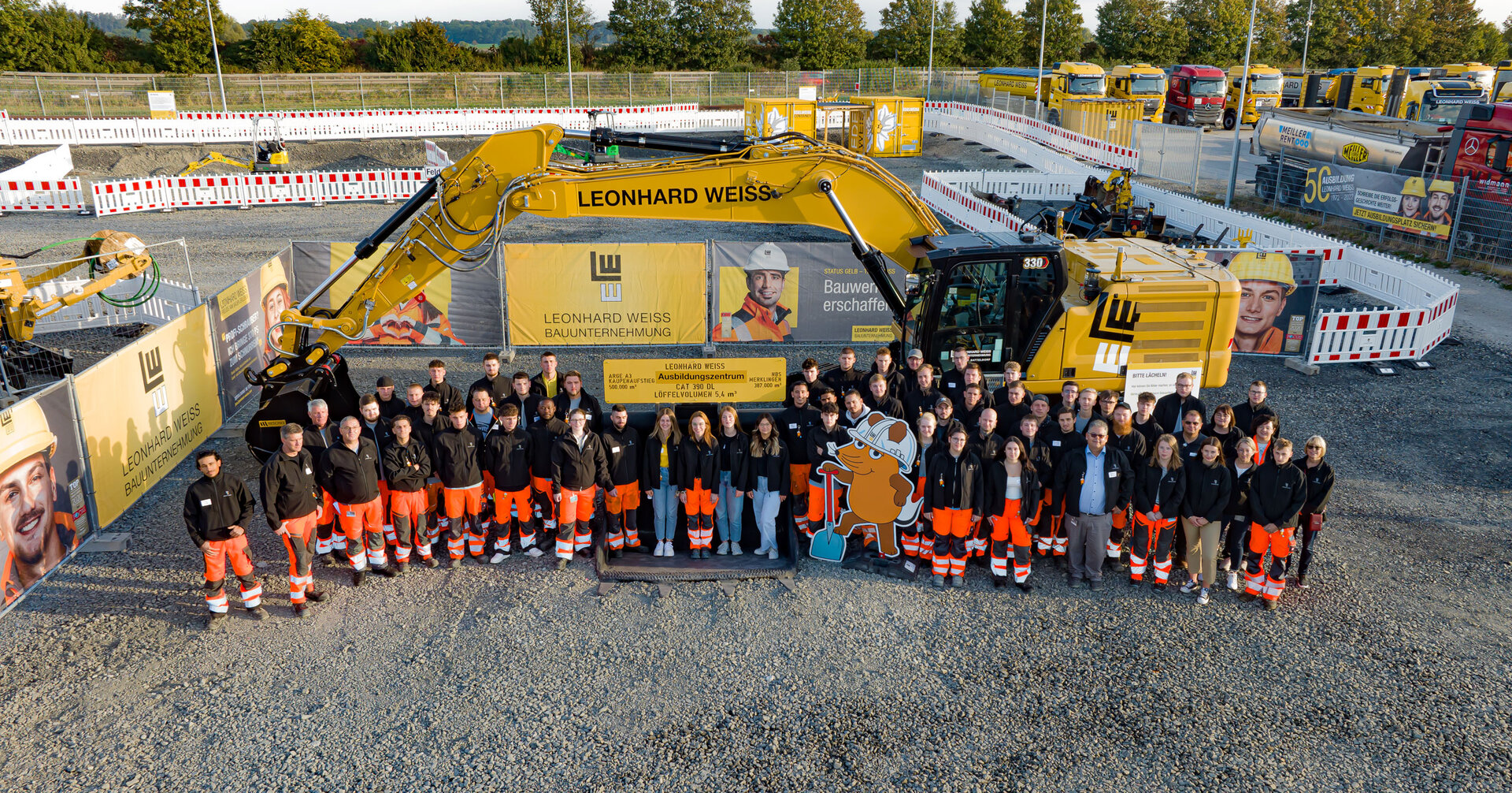 Gruppenfoto mit Auszubildenden und Ausbildern vor einem gelben Bagger auf dem Außengelände des Trainingszentrums