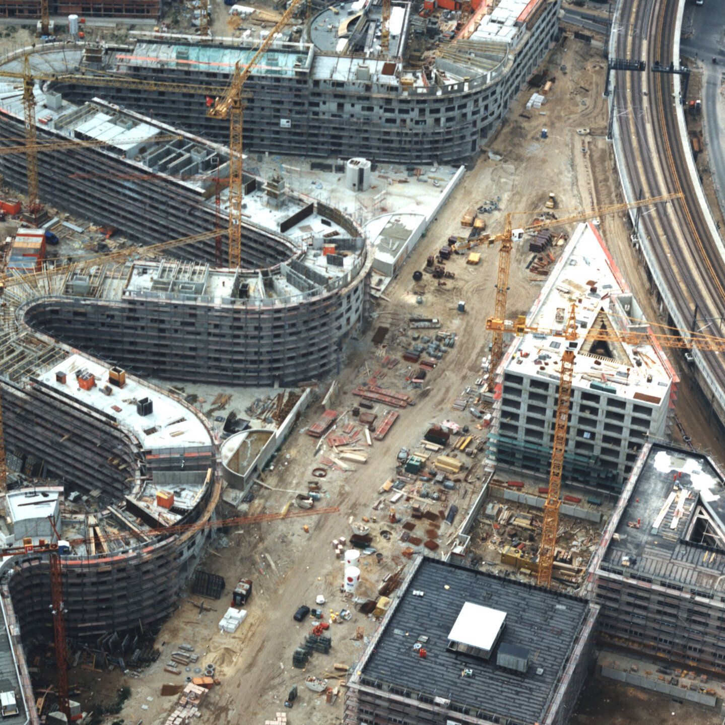 Aerial view of the Moabiter Werder construction site in Berlin. Several buildings in various construction phases, surrounded by construction cranes, a railway line and urban infrastructure