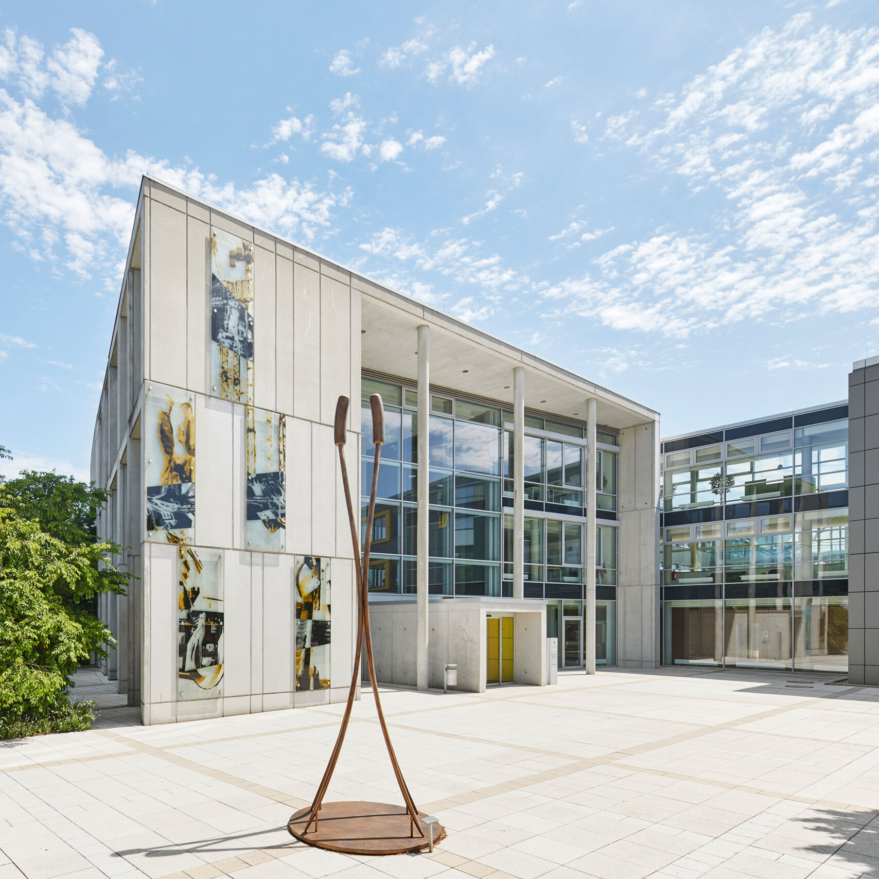 Modern building complex at the LEONHARD WEISS site in Göppingen with glass façades, artistic concrete walls and a sculpture on a sunny square