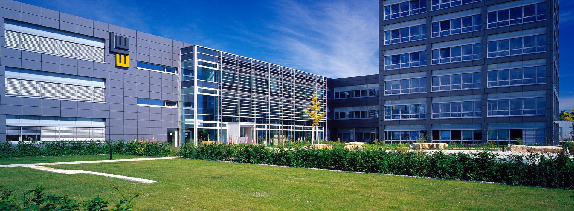 Außenansicht des Bürogebäudes am Standort in Satteldorf mit Glasfassade und grüner Rasenfläche