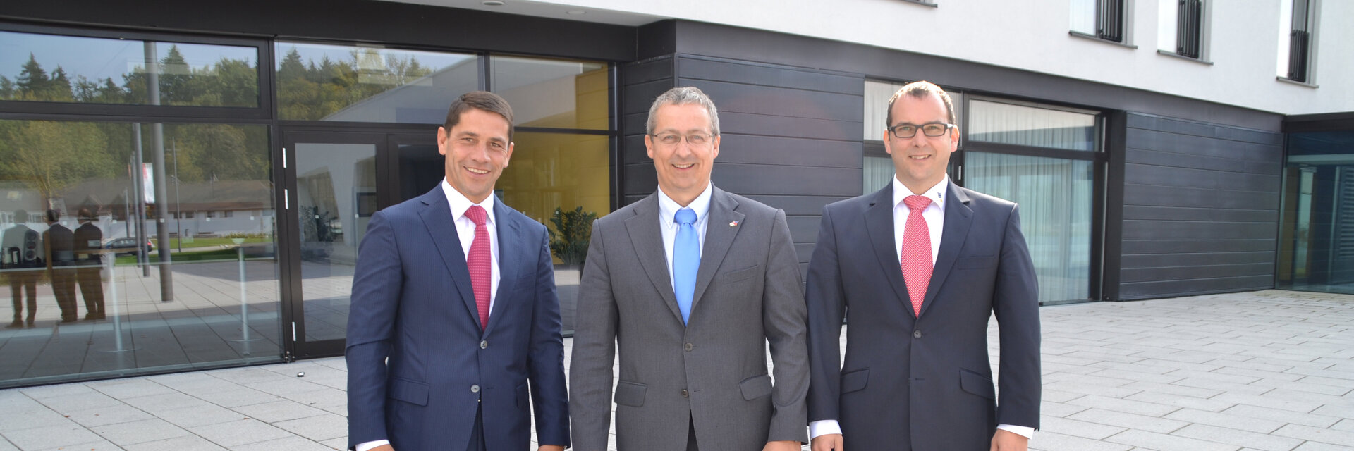 The 2014 shareholders, three men in suits and ties, walk towards the camera in front of the office building in Göppingen