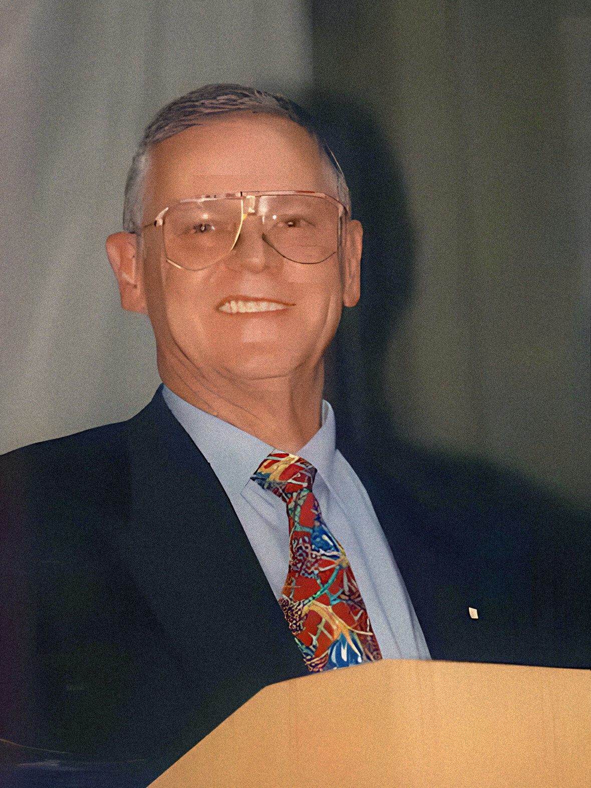 Werner Schmidt-Weiss stands smiling behind a lectern, wearing a suit and colourful tie